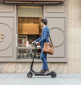 A young business man riding an electric scooter downtown